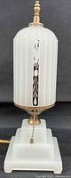 Front view showing entire lamp with milk glass body, base, pull chain and finial