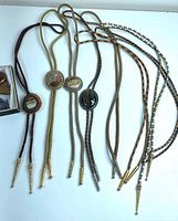 Group of seven bolo ties laid out showing cords, slides and metal tips