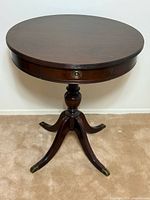 Full view of round mahogany pedestal table showing drawer pull, pedestal and legs