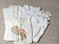 Group of folded white christening gowns with bonnet, shoes, brush