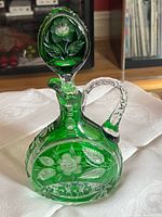 Front view of green cut glass decanter with stopper showing floral cut pattern
