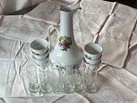 group shot of porcelain pitcher, cups stacked, and six etched glass mugs
