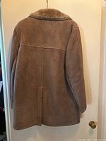 Rear view of brown shearling coat hung on door