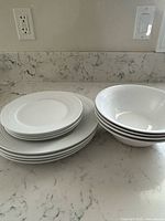 Stack of four large dinner plates, four smaller plates, four regular bowls, and four soup bowls shown on marble countertop.