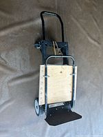 Full view of black metal frame hand truck trolley with wooden base and metal foot plate, two wheels.
