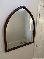 Full view of the arch cathedral wall mirror showing the brown wood frame and reflective clear mirror glass in a home entryway setting.