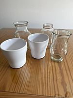 Front view of all 5 vases on wooden surface showing ceramic and glass materials