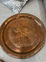 Close-up photo of a brass bar plate with embossed design showing a man in top hat and cane with lettering around the edge.