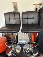 Two black leather adjustable bar stools with tufted seat and backrest, chrome base with footrest.