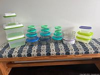 Wide view of all 20 containers arranged in a row on a table, showing various plastic, glass, and metal containers with lids in different colors and sizes.