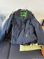 Front side of a dark winter coat with visible pockets, collar, and adjustable belts at the bottom.