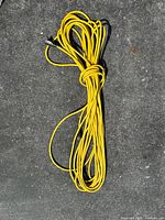 Coiled yellow extension cord on pavement, shows overall length and condition.