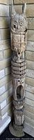 Full length front view of the wooden owl totem pole leaning against a brick wall