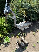 Full side view of the metal handcrafted stork sculpture standing in garden soil with greenery background.