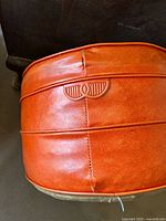 Close-up photo of the side outer surface showing orange leather, horizontal stitching and a visible seam split indicating minor damage.