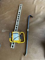 Metal spirit level, aluminum crowbar, and yellow portable halogen light laid side by side on brown surface
