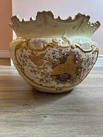 Front view of the porcelain chamber pot showcasing gilt bird and nest artwork with floral patterns and raised textured ceramic base.