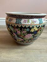 Side view of porcelain planter pot showing colorful floral and butterfly designs on black background with a decorative white rim.