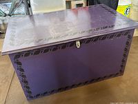 Front view of purple hand painted chest with black leaf border, metal latch on front, scratches and wear visible on top surface.
