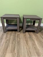 Two gray wood side tables placed on a wooden floor against a green wall.
