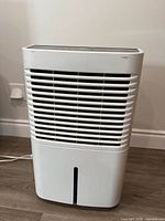 Front view of white Whirlpool dehumidifier showing air intake grill and water bucket window at the base.