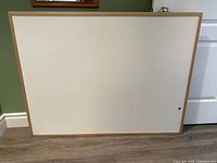 Front view of the large whiteboard with wooden frame placed standing against a green wall and white door, showing overall condition and design.