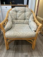 Front view of a wicker armchair with a patterned, tufted cushion featuring paisley designs.