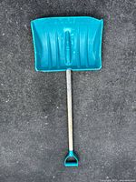 Winter shovel with turquoise plastic snow blade, wood handle and turquoise plastic D-grip handle lying on pavement
