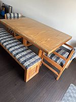 Full dining set from an angle showing table with wood top and glass overlay, bench and chairs with geometric upholstery