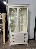 Front view of painted white china cabinet showing glass-paneled doors and lower drawers