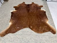 Full view of brown cowhide rug spread out on floor, showing natural shape and texture.