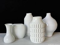 Group of six modern white ceramic vases displayed against black background to show shapes and size variations.