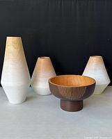 Four turned wood vases in natural shades with white washed bottoms and a decorative wooden bowl with dark exterior and vertical line pattern.
