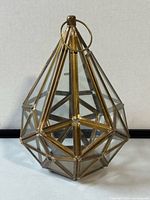 Front view of geometric brass and glass hanging lantern candleholder showing faceted glass panels and brass frame with hanging ring.