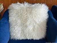 Front view of ivory Mongolian sheepskin pillow on blue armchair, showing soft curly texture and fullness.