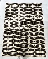Top down full view of the large rectangular area rug with brown background and cream geometric pattern, showing entire rug shape and design.