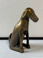 Front left view of the brass dog figurine showing its shape and smooth brass surface with patina.