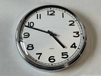 Front view of the wall clock showing the chrome frame, white face, black numbers and hands, and quartz label.