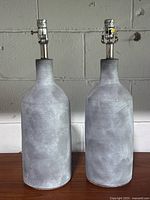 Pair of grey cement-finished bottle table lamps side by side showing the full shape and lamp fitting on top