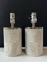Pair of white textured chevron-patterned cylindrical table lamp bases with chrome socket hardware, front view.