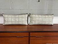 Front view of two rectangular grey and cream patterned lumbar pillows on wood surface with light pilling visible on fabric.