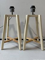 Front view of both lamps showing cream legs and natural wood crossed bases with metal lamp fittings on top.