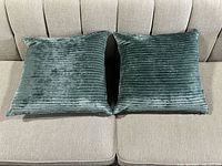 Pair of teal velvet ribbed throw pillows shown on a beige couch, displaying overall size and condition.