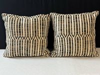 Two matching square pillows with a vertical geometric pattern, cream and dark earth tones, displayed side by side.