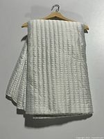 Folded quilted satin coverlet hanging on a hanger showing vertical stitch pattern and satin sheen.