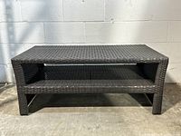 Front view of the rectangular resin wicker outdoor patio table showing dark brown woven wicker and a lower shelf.