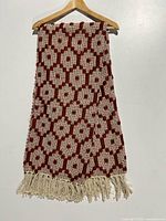 Full view of the rust and cream geometric woven throw blanket folded on a wooden hanger against a white background, showing pattern and fringe.
