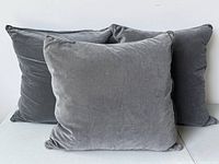 Three charcoal grey velvet throw pillows stacked showing front surfaces and size within a group