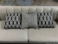 Set of three decorative throw pillows arranged on a gray couch. Two black and white geometric pattern pillows flank a navy and white Greek key pattern pillow.