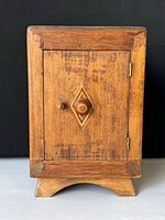 Front view of small antique wooden cabinet showing door with wooden knob and diamond inlay pattern.